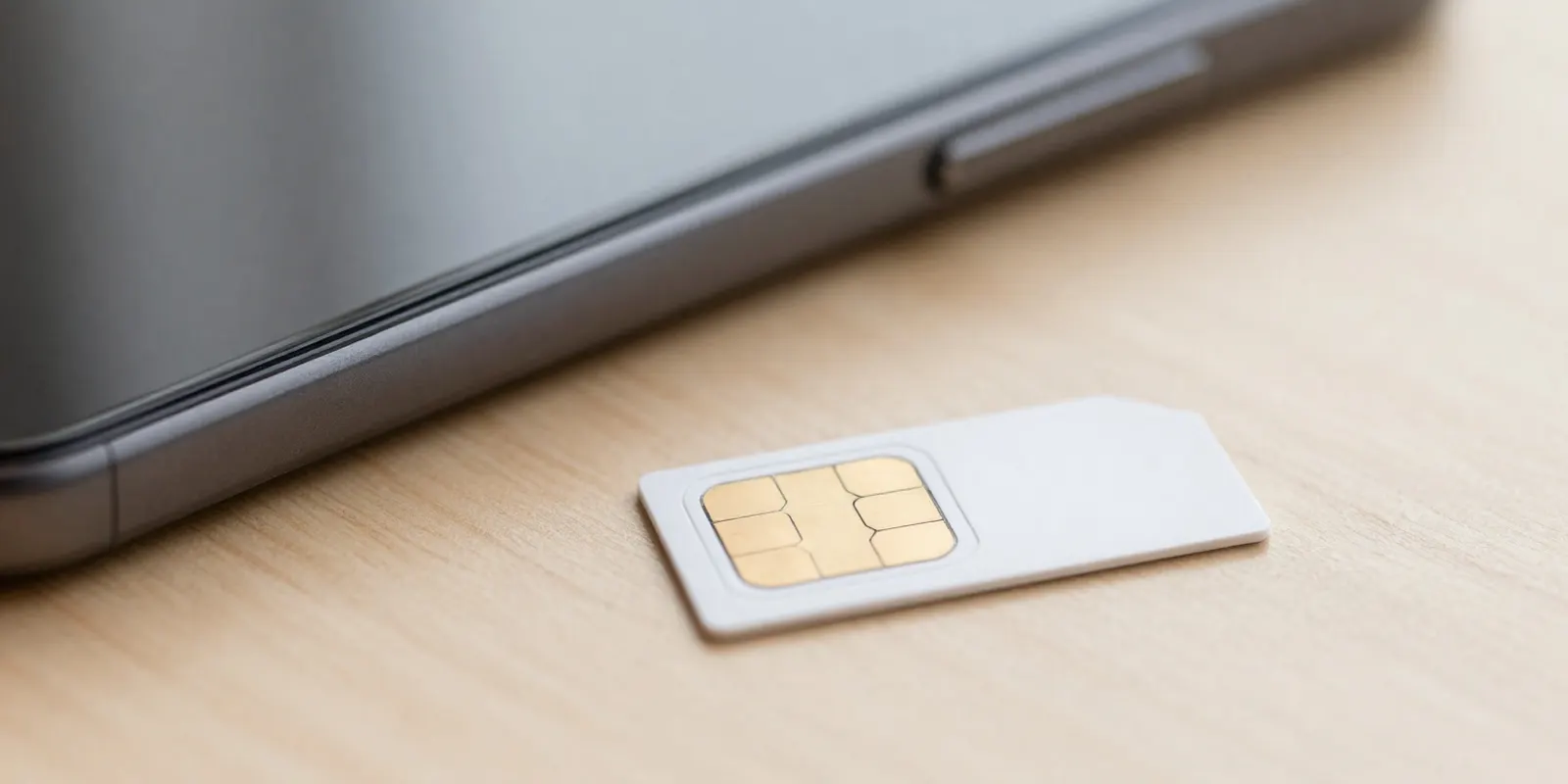 A physical SIM card on a desk next to a smartphone