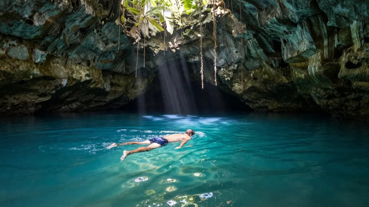 A swimmer in a turquoise cenote lit by sunlight from an opening above